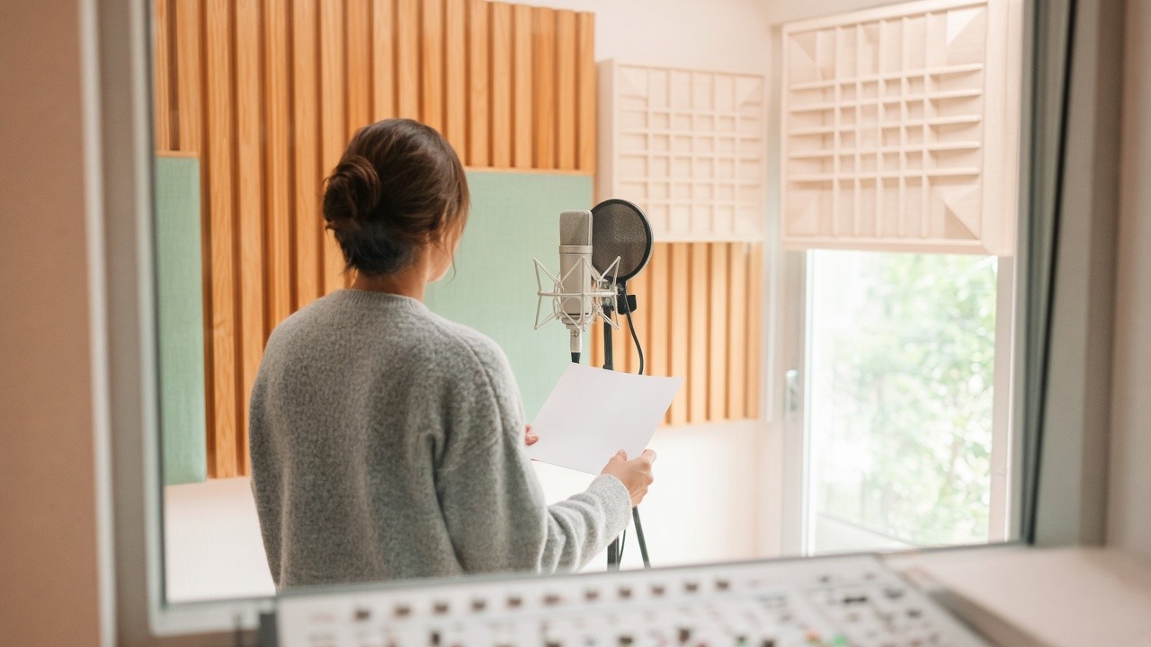 A vocal session seen through the glass of a recording booth.